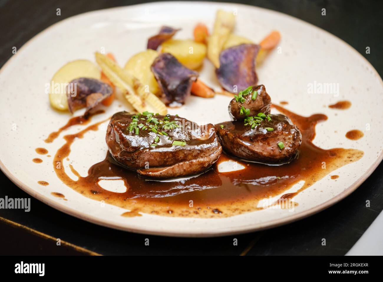 High angle of delicious grilled beef medallions served with potatoes carrots and baby corns decorated with sauce and green onion and served in restaur Stock Photo