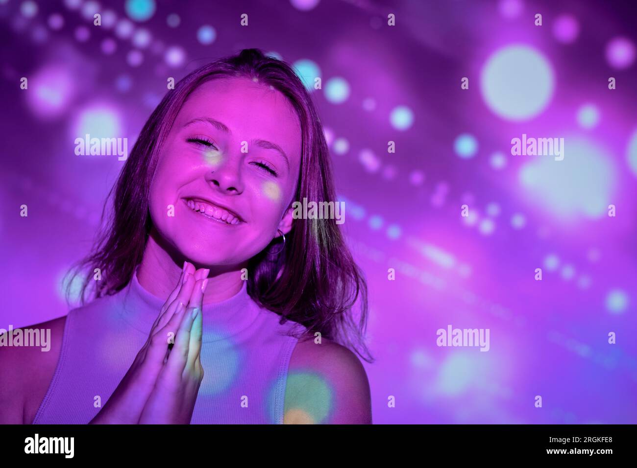 Happy young woman clasping hands and smiling gleefully while making ...