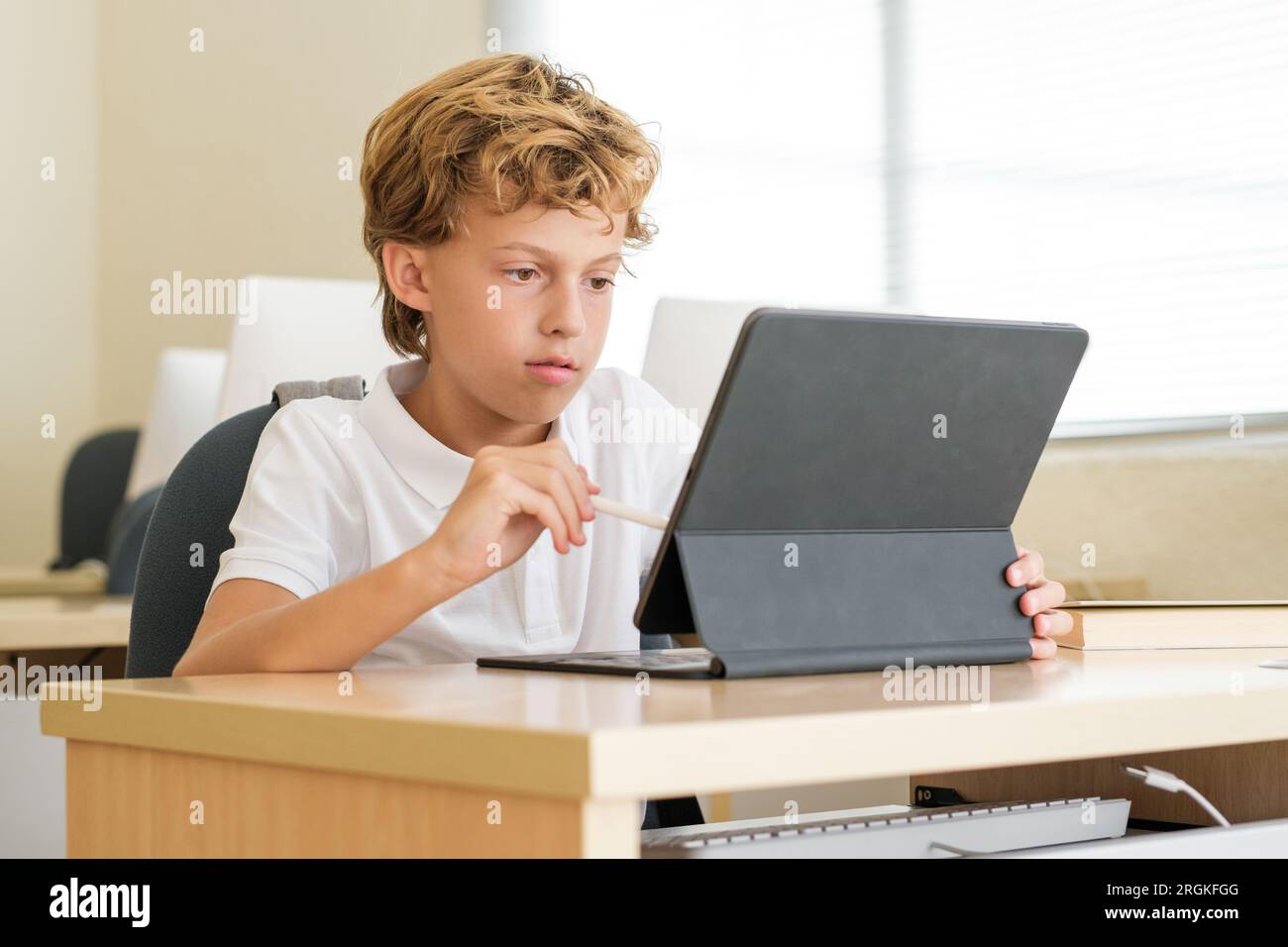 Intelligent schoolkid using stylus on tablet while studying in modern classroom at school Stock Photo