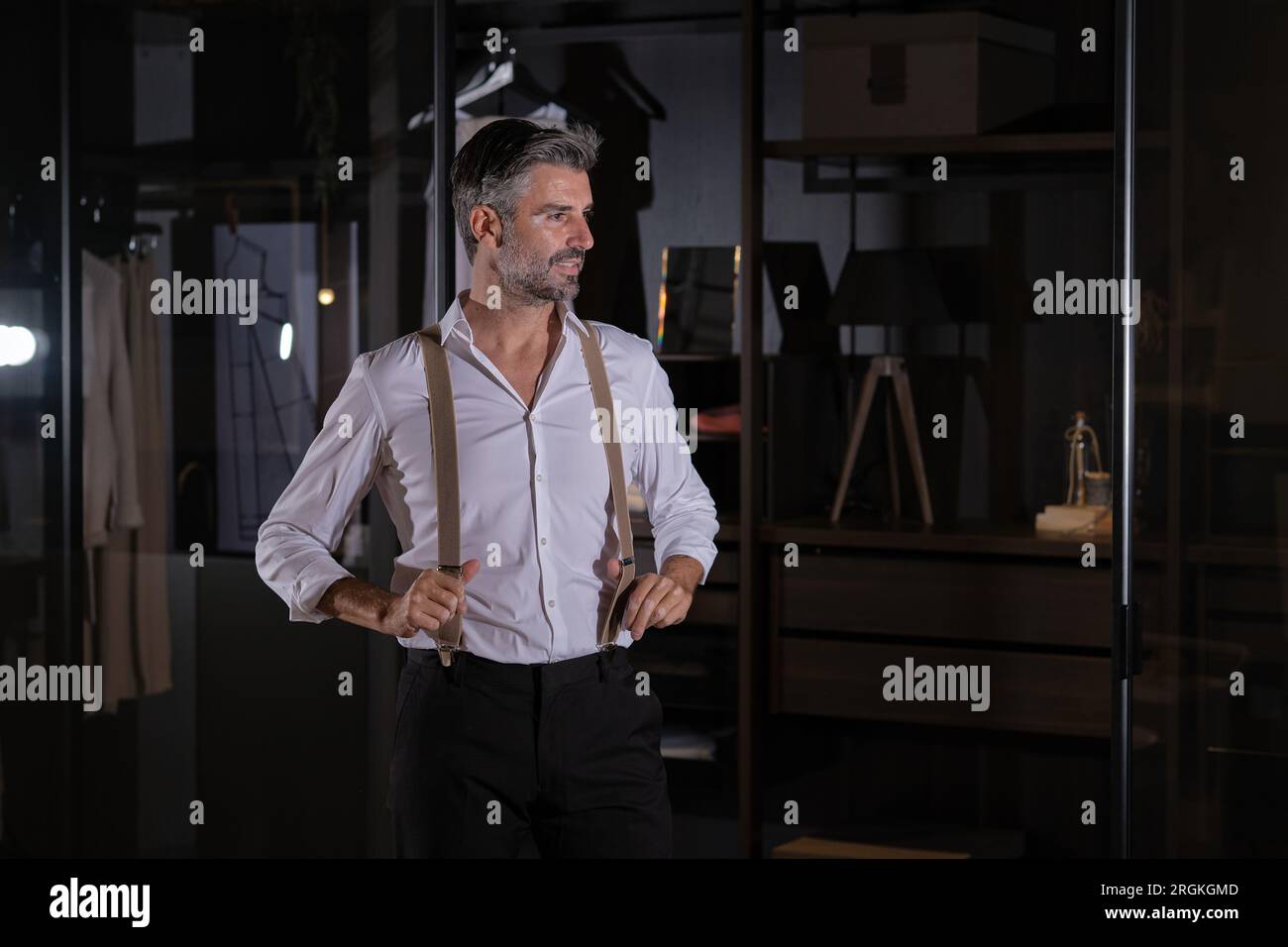 Middle aged confident handsome smiling bearded mature man standing straight with hands on beige suspenders Stock Photo