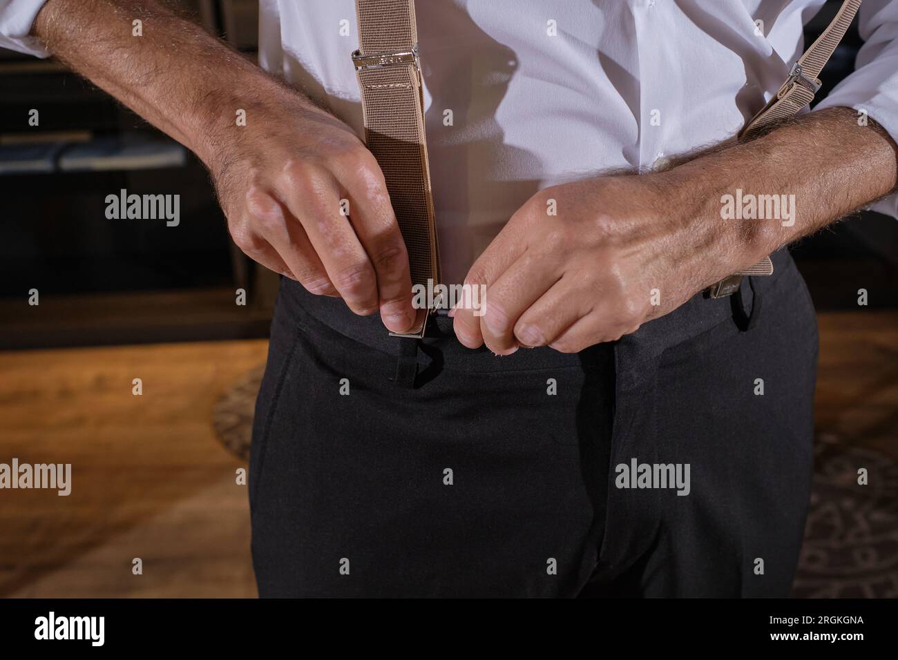 Crop anonymous male model in formal clothes putting on clip suspenders and choosing new outfit while spending time in atelier Stock Photo