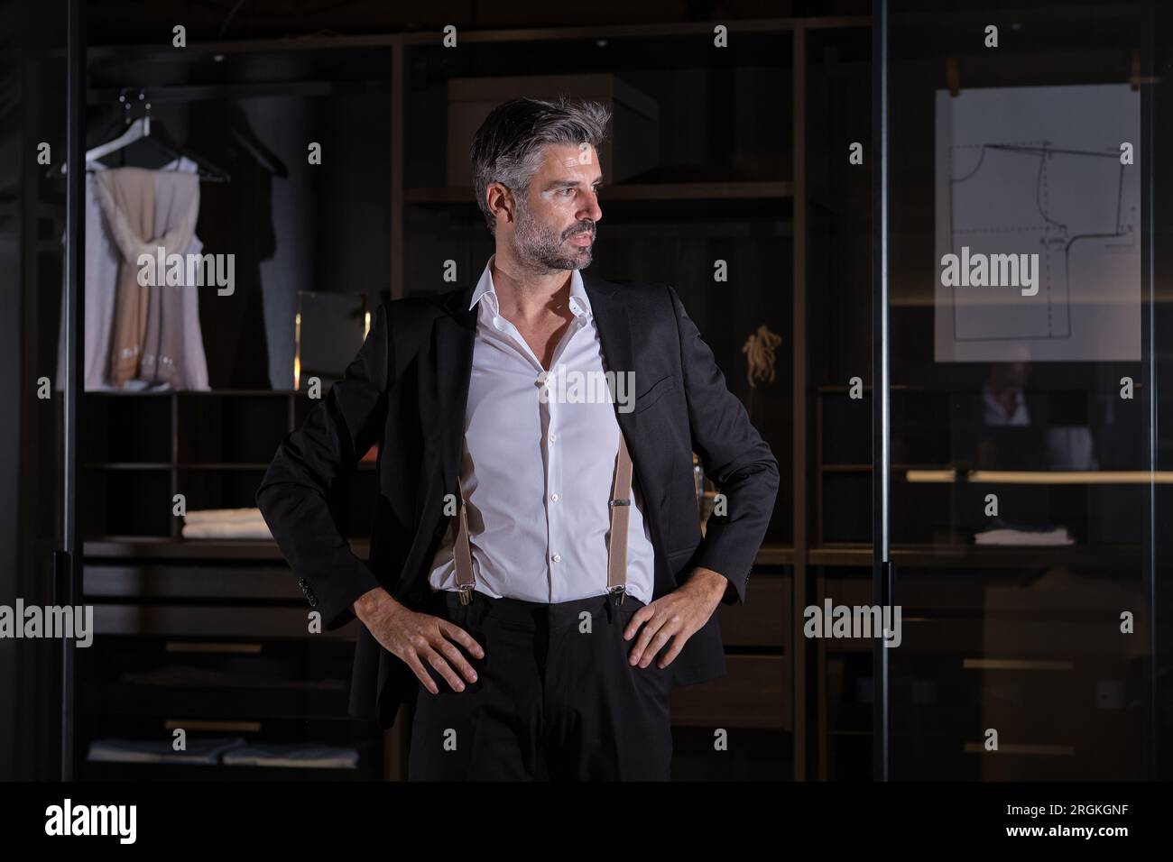 Adult middle aged male in elegant clothes standing against wardrobe and looking away with hands on waist Stock Photo