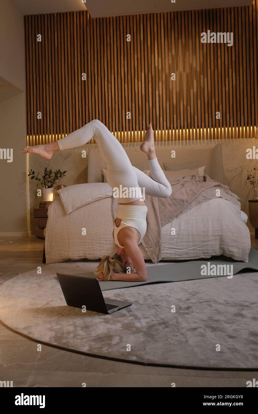 Full body of young female doing yoga in modern bedroom designed in pastel colors Stock Photo