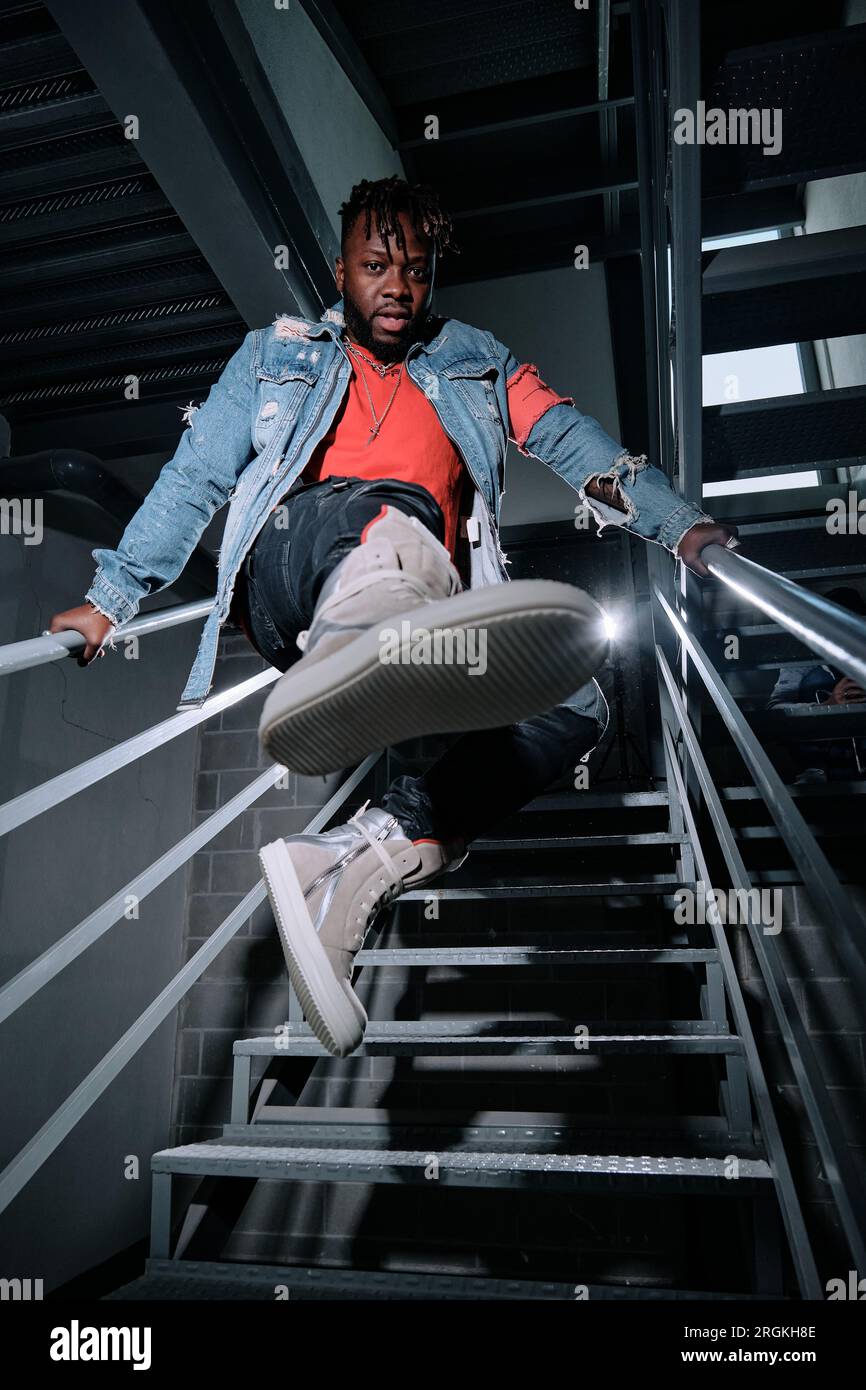 Full body of young ethnic male in trendy outfit and sneakers holding on ...