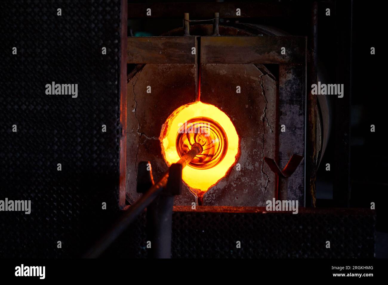 Glass object on tip of blowpipe placed in burning furnace in dark facility at glassblowing