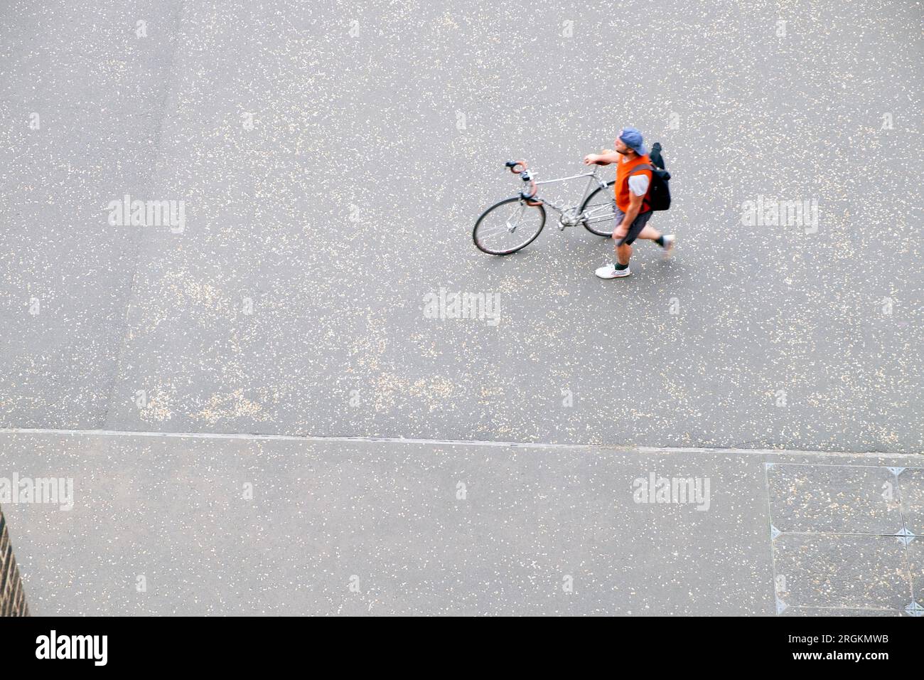 High view looking down on pavement with cyclist walking his bike