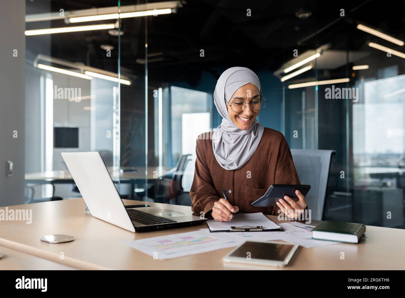 Muslim smiling young Dinka woman in hijab working in office with laptop ...