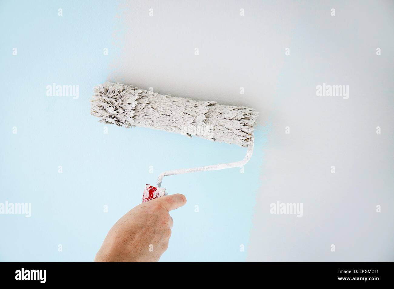 Man worker using paint roll to repaint old wall paint, rolling tool. Blue to neutral gray. Home indoors. Stock Photo