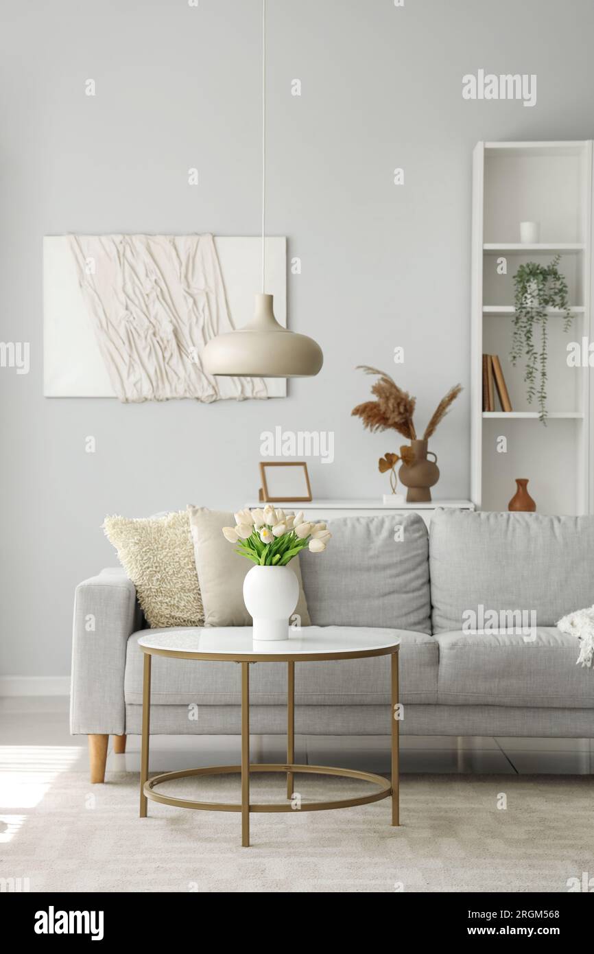 Cozy grey sofa and vase with tulip flowers on coffee table in interior ...