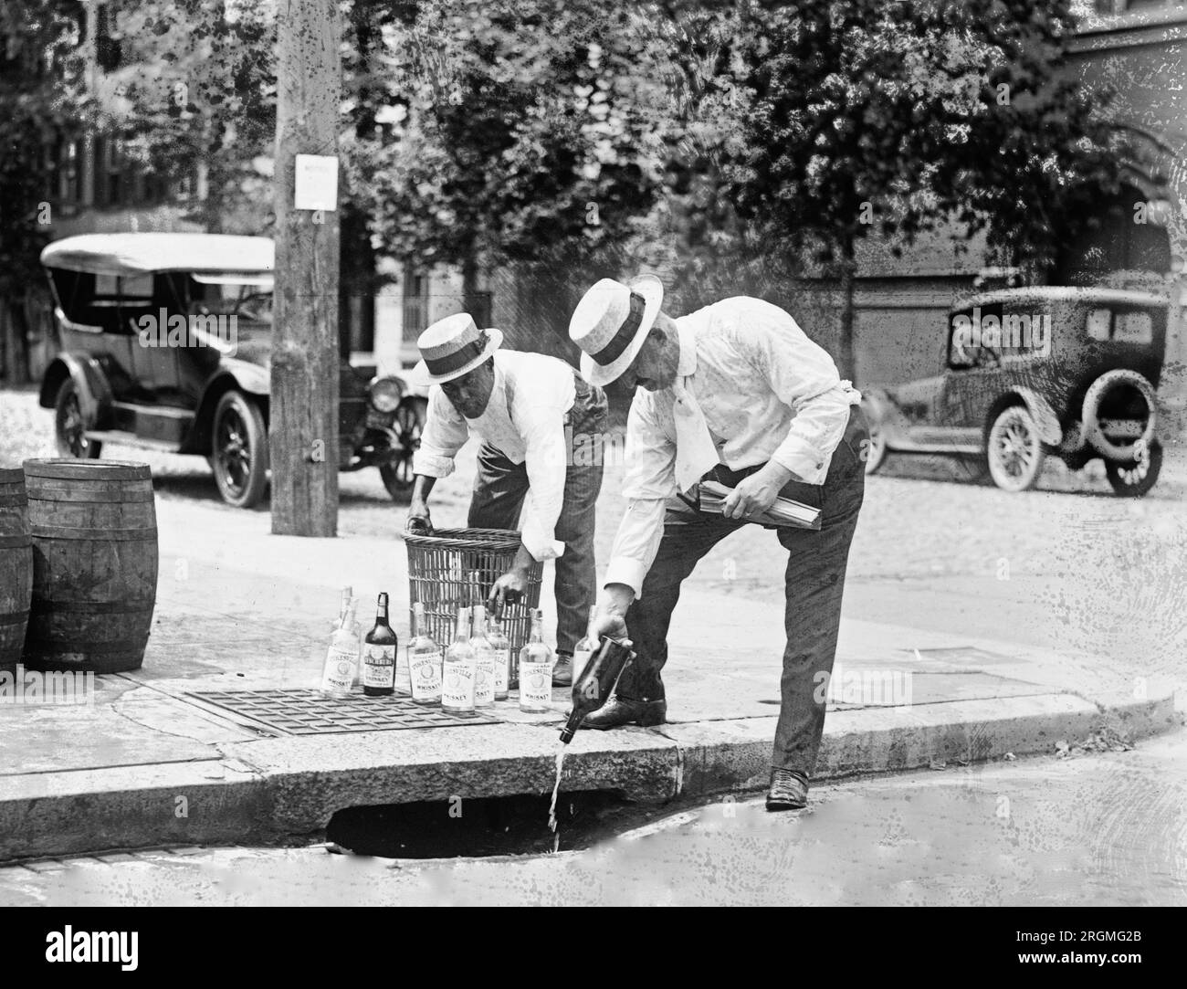 Two men pouring liquor into storm drain during prohibition ca. 1921