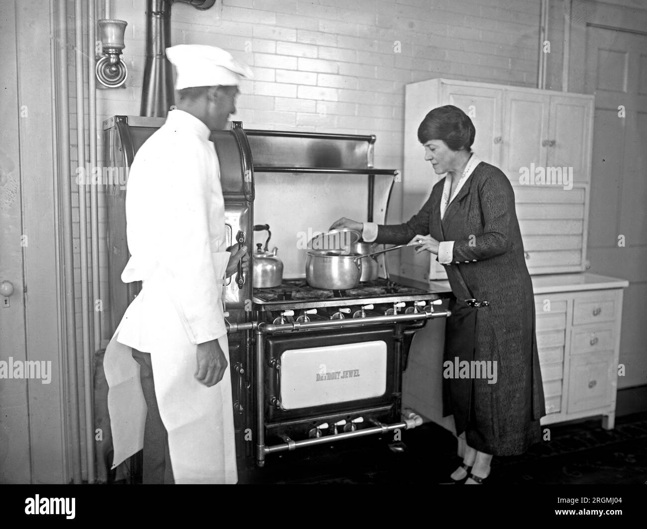 Mary Roberts Rinehart looking at a pot on a stove in a kitchen, and a chef ca. 1926 Stock Photo