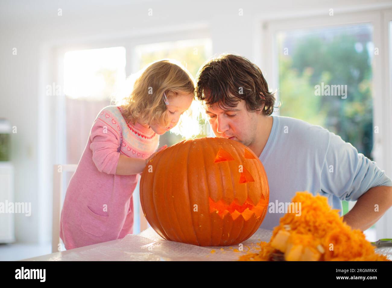 Father and child carving pumpkin for Halloween. Dad and little girl carve jack-o-lantern for trick or treat and home entrance decoration. Stock Photo