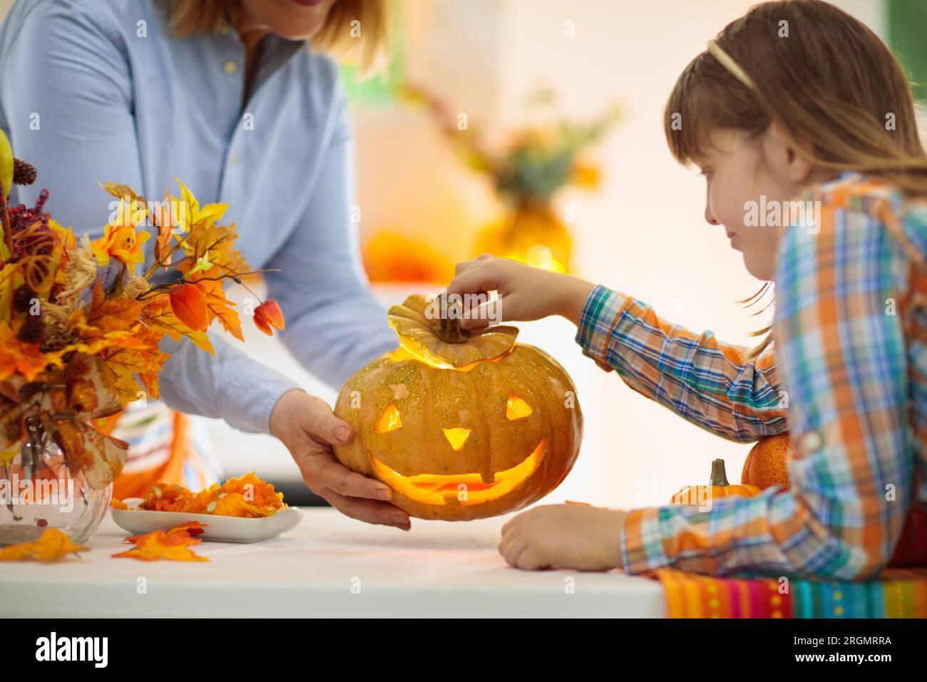Family carving pumpkin for Halloween celebration. Woman and little girl cutting jack o lantern for traditional trick or treat decoration. Stock Photo