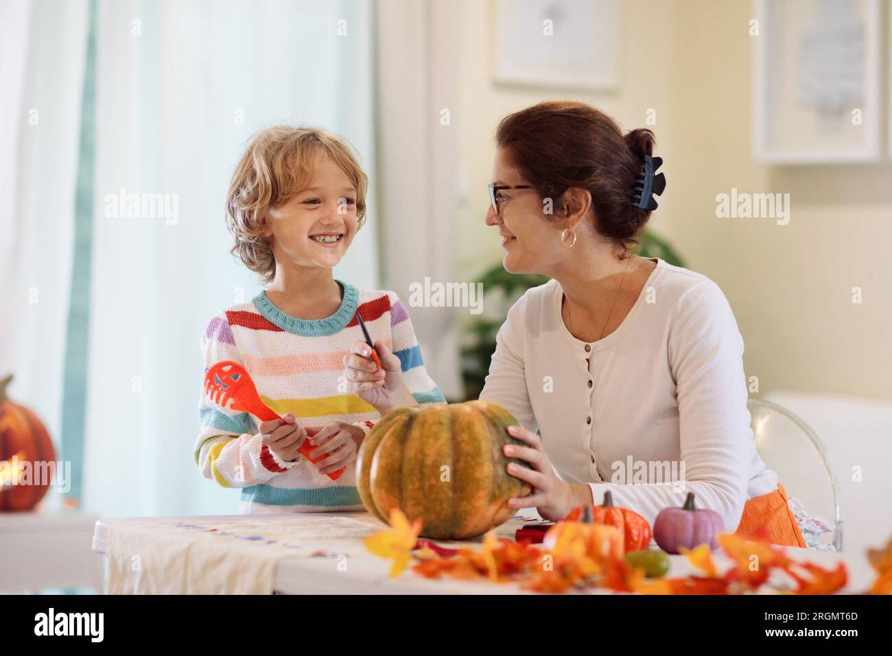Family carving pumpkin for Halloween celebration. Woman and little boy cutting jack o lantern for traditional trick or treat decoration. Mother and ch Stock Photo