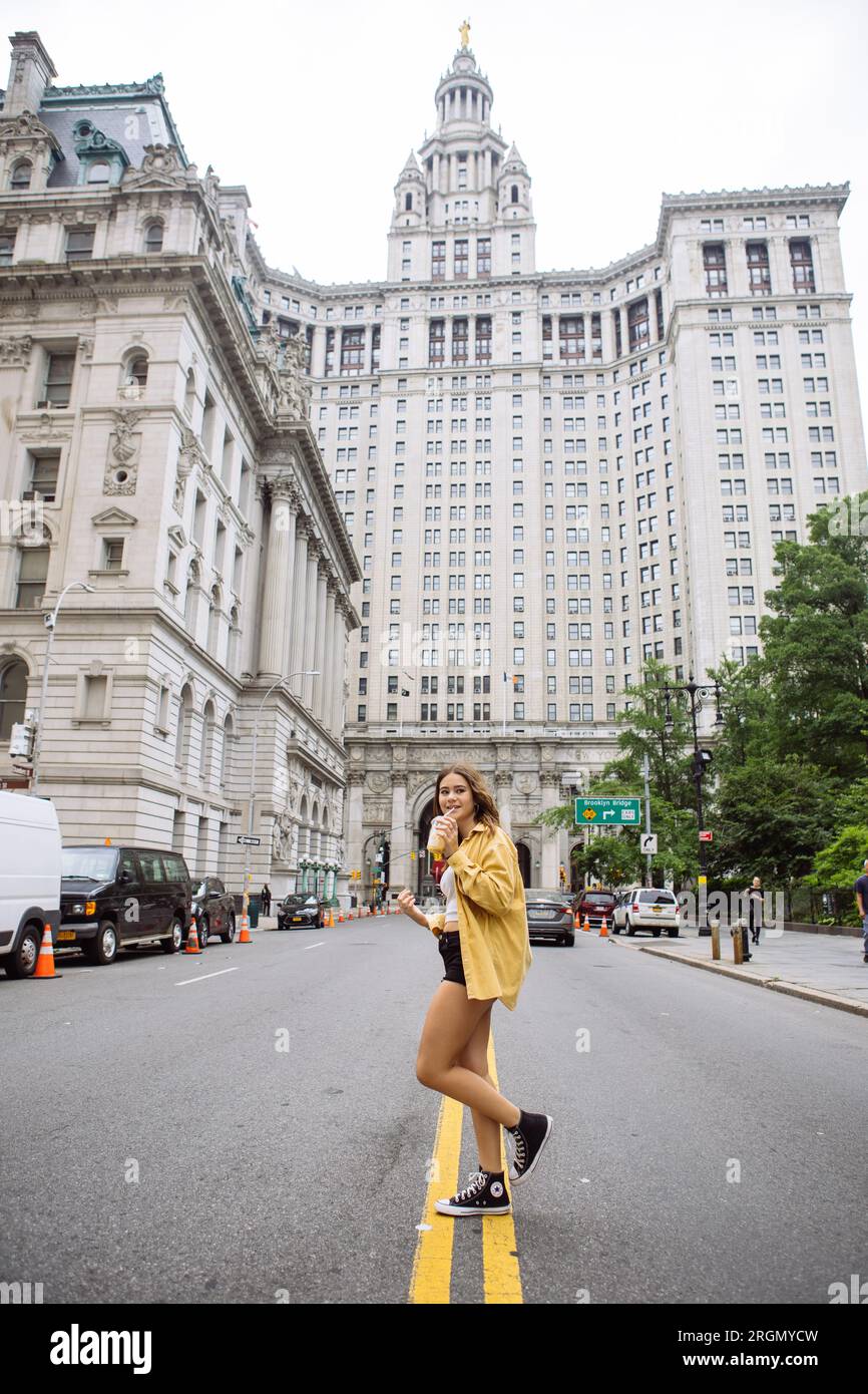 Young girl posing in the middle of a Manhattan street drinking a coffee with the Manhattan Municipal Building in the back Stock Photo