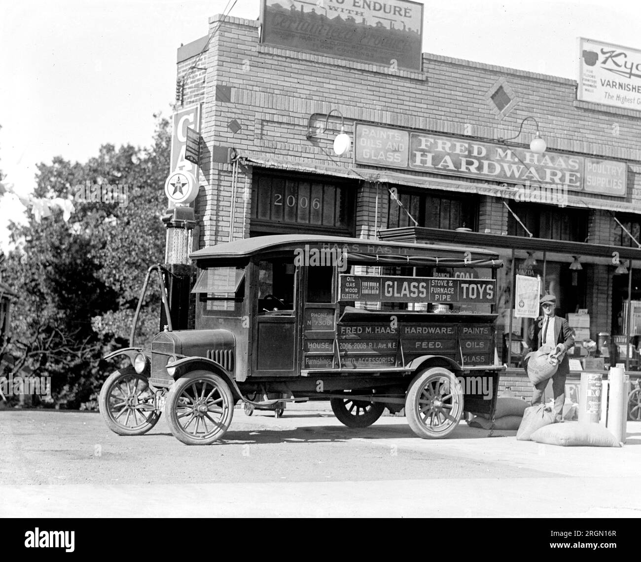 A delivery truck parked in front of a gas station and hardware store ca. 1924 Stock Photo