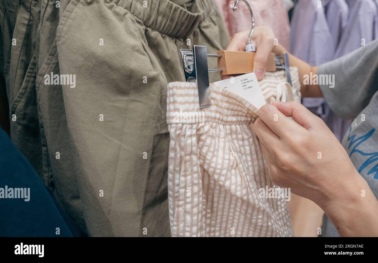 Woman shopping cotton shorts in clothing store. Woman choosing clothes. Shorts on hanger hanging on rack in clothing store. Fashion retail shop inside Stock Photo