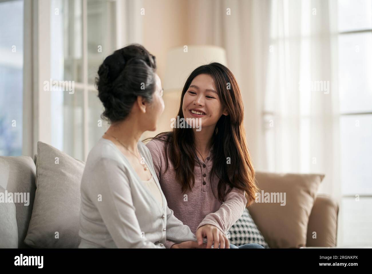asian adult daughter sitting on couch at home chatting conversing with senior mother happy and smiling Stock Photo