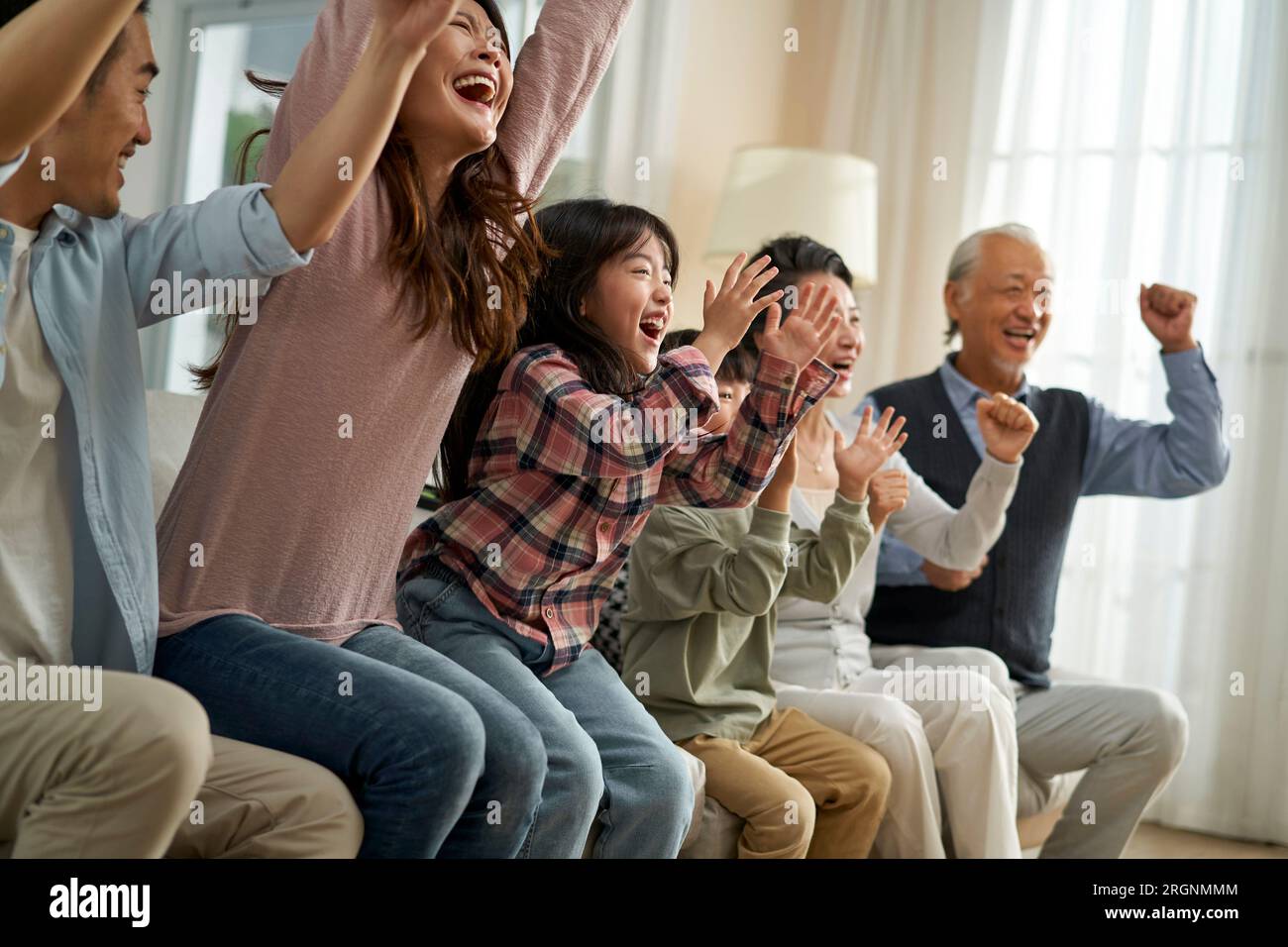 three generation asian family watching soccer game telecast on tv together at home Stock Photo