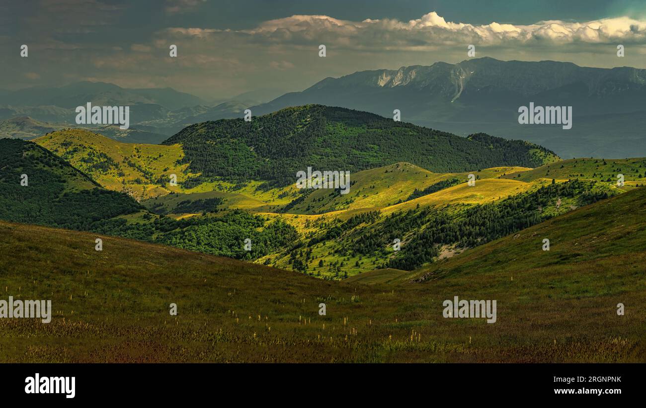 Mountainous landscape with woods and prairies illuminated by patches of oblique light. In the background the Sirente massif. Abruzzo Stock Photo