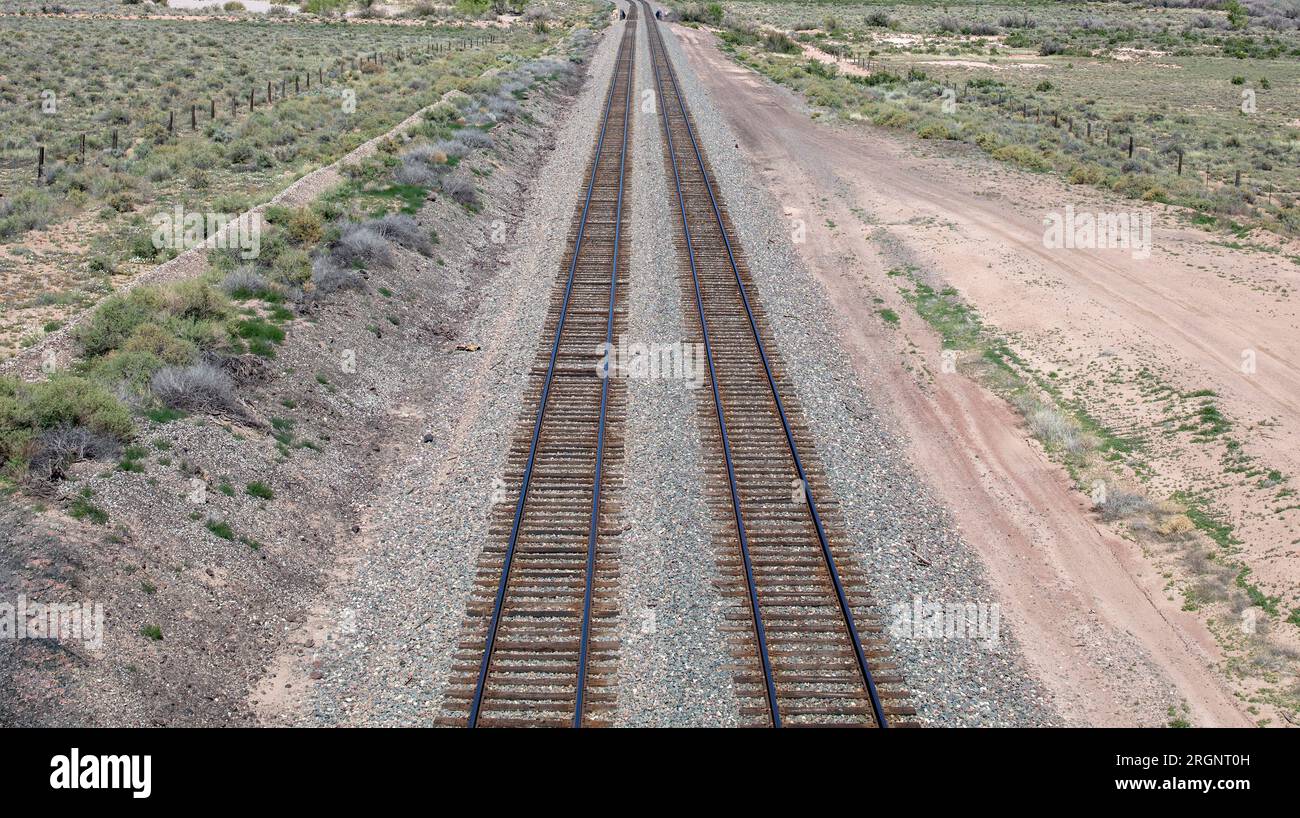 Railroad track in countryside crossing desert with low vegetation background, USA Arizona. Empty steel railway with gravel and fence at side. Above vi Stock Photo