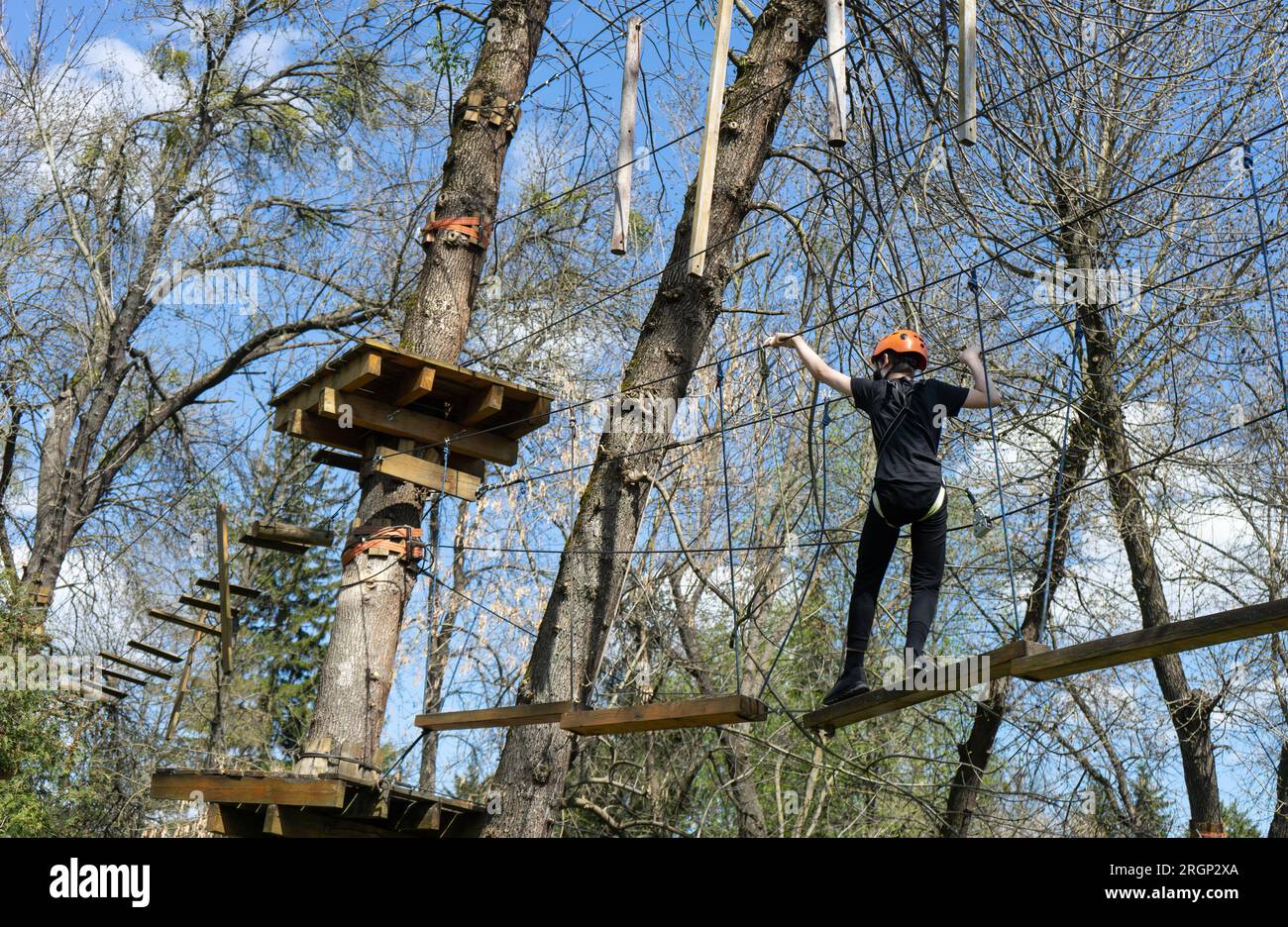 boy climb or walk on high rope trail in adventure park Stock Photo