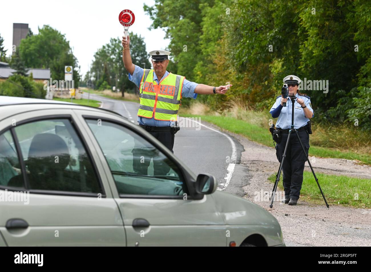 11 August 2023, Saxony-Anhalt, Zörbig: Police Captain Wolfram Barthel waves out a vehicle that Police Captain Peggy Schmidt measured was speeding in a 30-mph zone. The Saxony-Anhalt police are taking part in the Europe-wide Roadpol speed week. The association of traffic police forces in the member states of the European Union aims to improve safety on European roads. Photo: Heiko Rebsch/dpa Stock Photo
