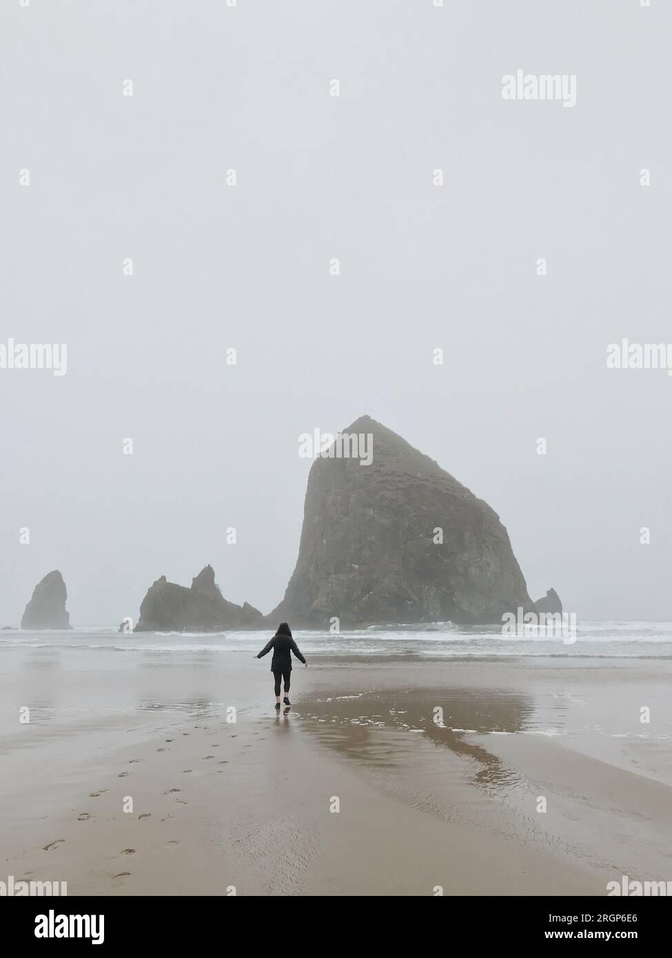 Woman jogging towards ocean on rainy beach. Stock Photo