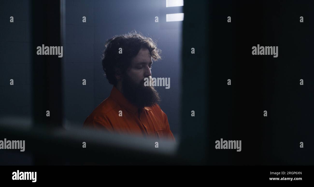 Believing male prisoner in orange uniform kneels near the bed, prays to ...