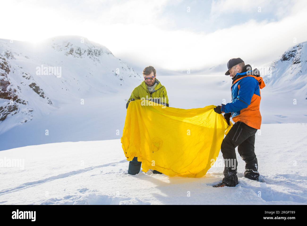 Two men unfold a yellow emergency shelter Stock Photo