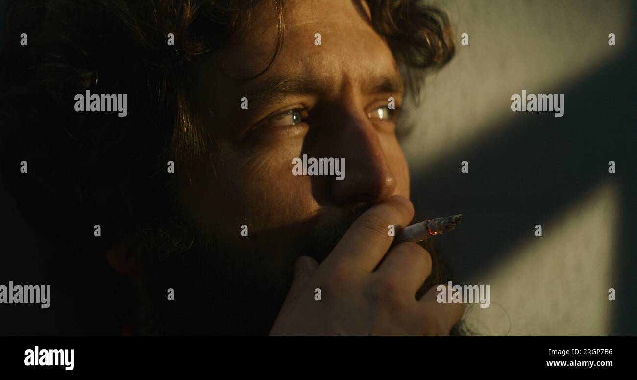 Depressed prisoner in orange uniform sits in prison cell, smokes