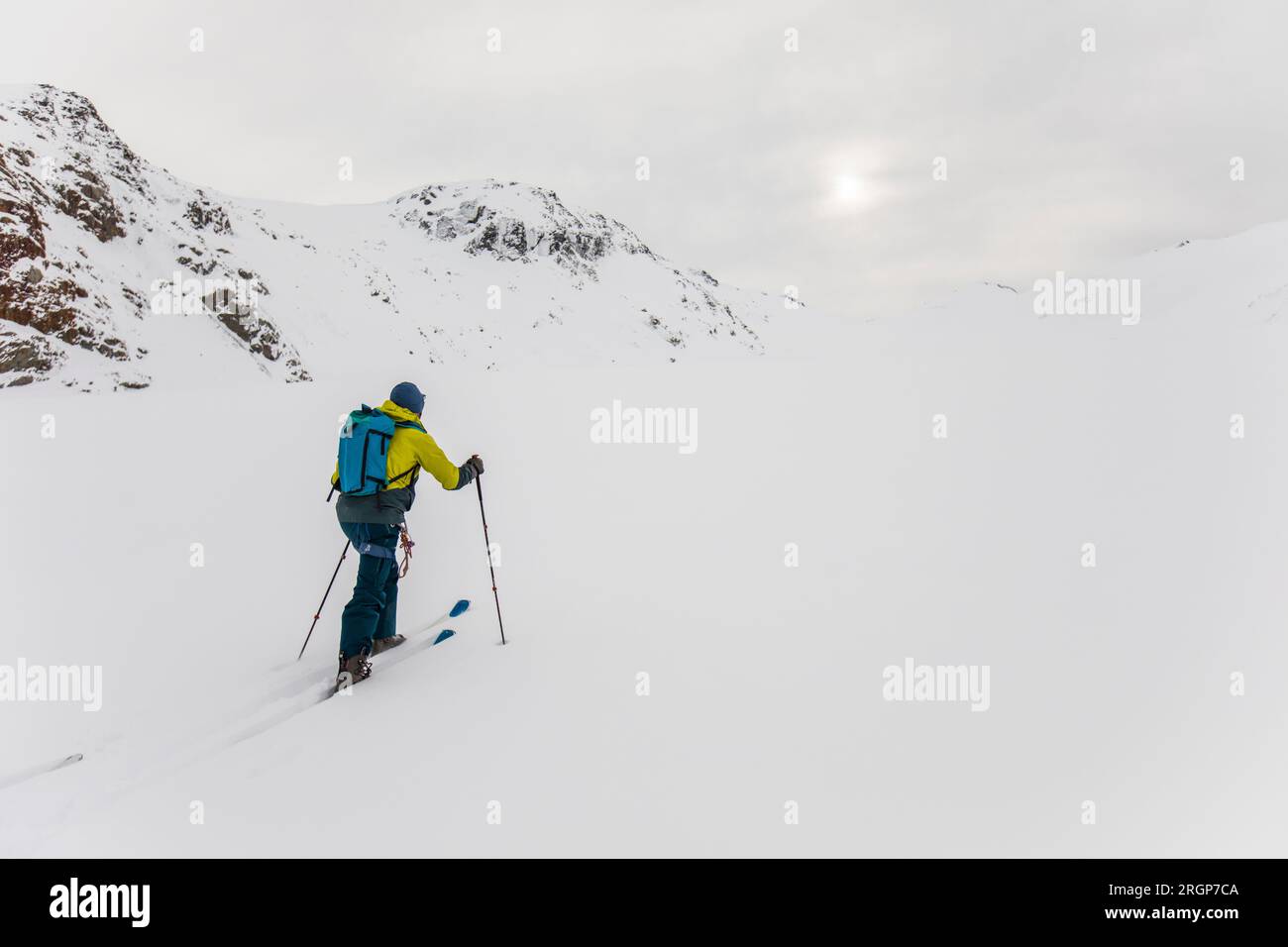 Rear view of man ski touring up mountain in B.C. Canada Stock Photo