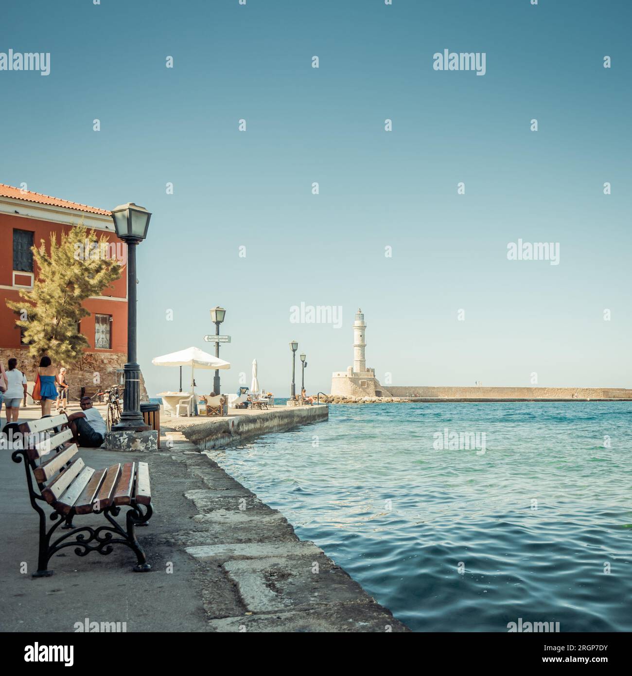 sea promenade in Chania port with a view at lighthouse and breakwater. Few benches with a view at the harbor placed along the embankment. Stock Photo