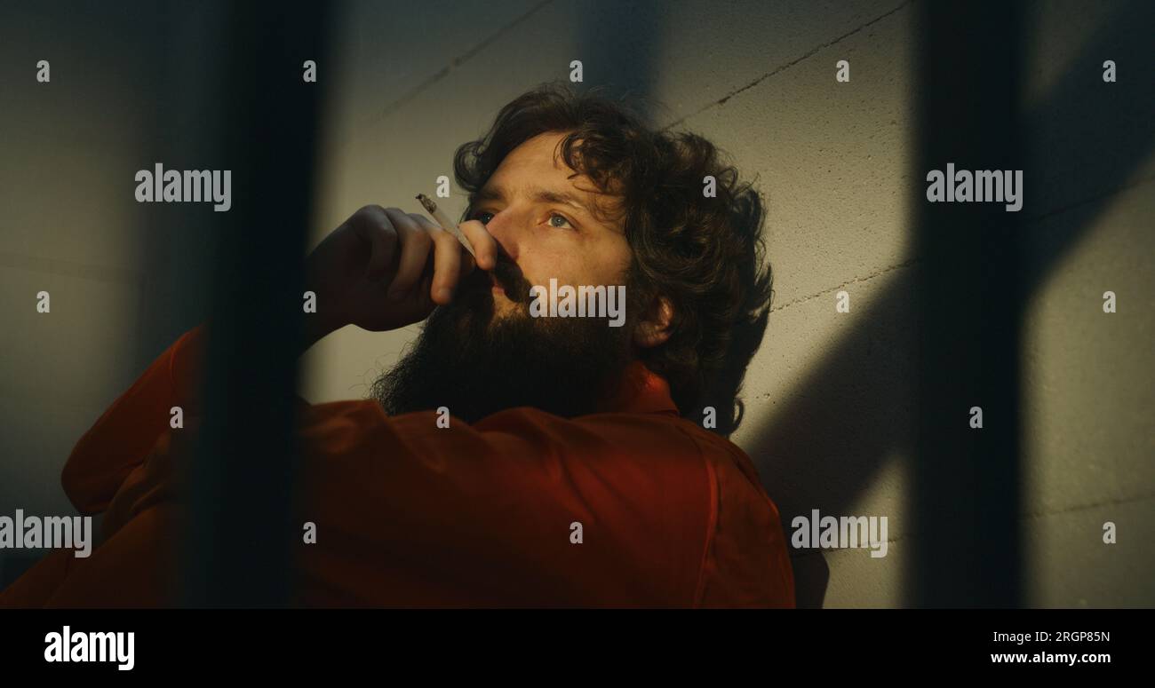 Thoughtful male prisoner in orange uniform sits on the bed, lights