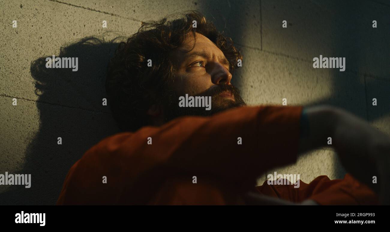 Depressed prisoner in orange uniform sits on bed in prison cell, smokes