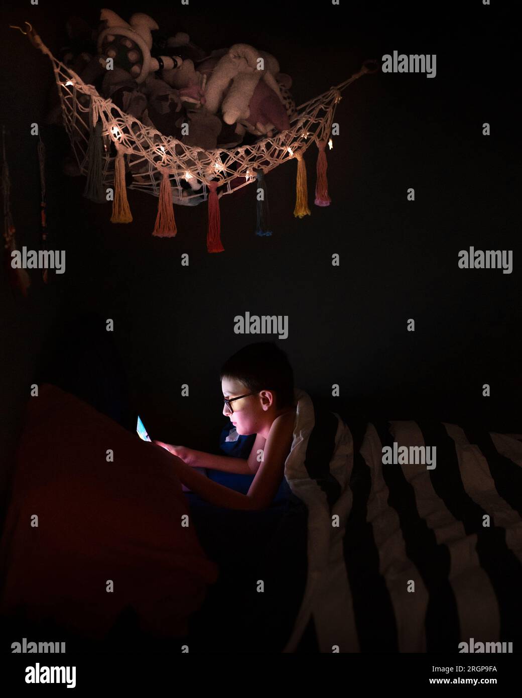 A boy playing his tablet in the dark in his bedroom Stock Photo