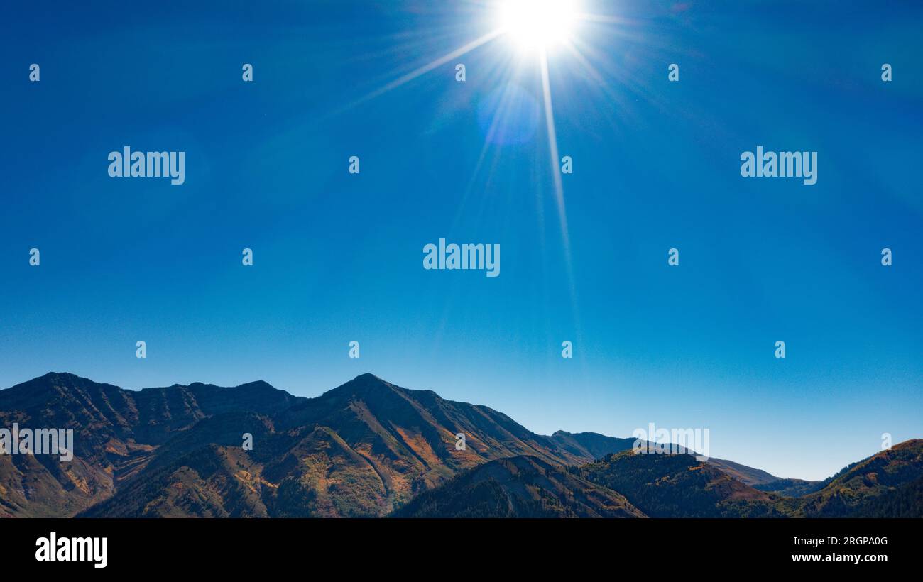 Sun shine and rays in middle of afternoon blue sky over mountain peaks Stock Photo