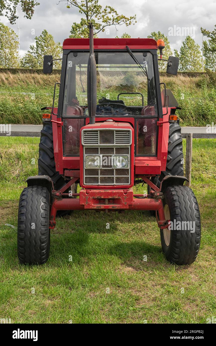 red colored farm tractor is parked on a pasture Stock Photo