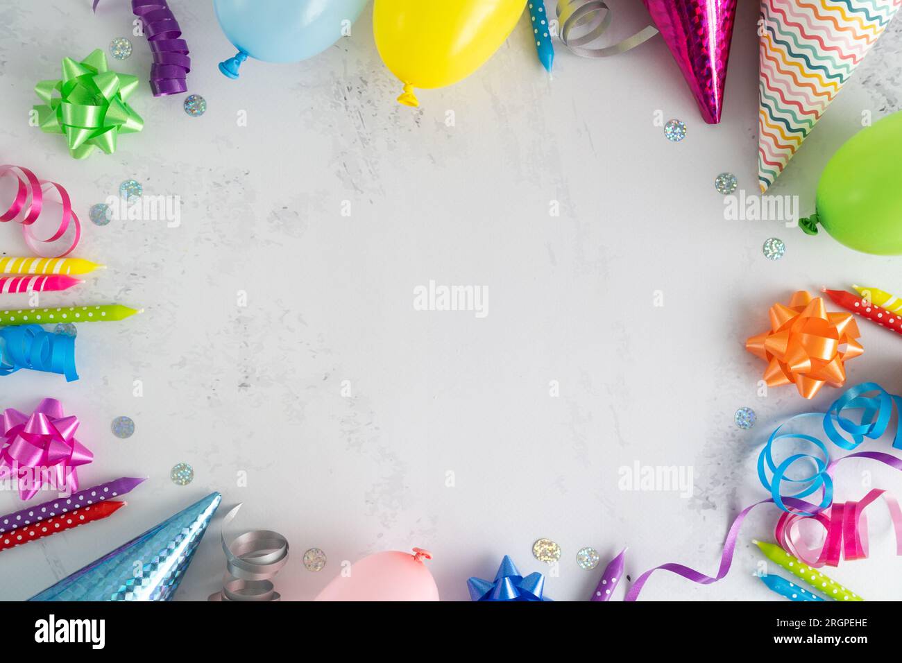 Birthday party flat lay composition frame. Colorful balloons, cake candles, cone hats, bows, ribbons decorations. Invitation concept with copy space. Stock Photo