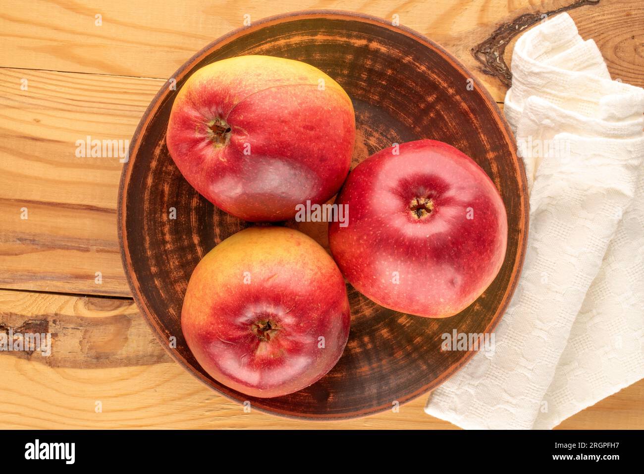 Three organic juicy apples with clay plate on wooden table, macro, top view. Stock Photo