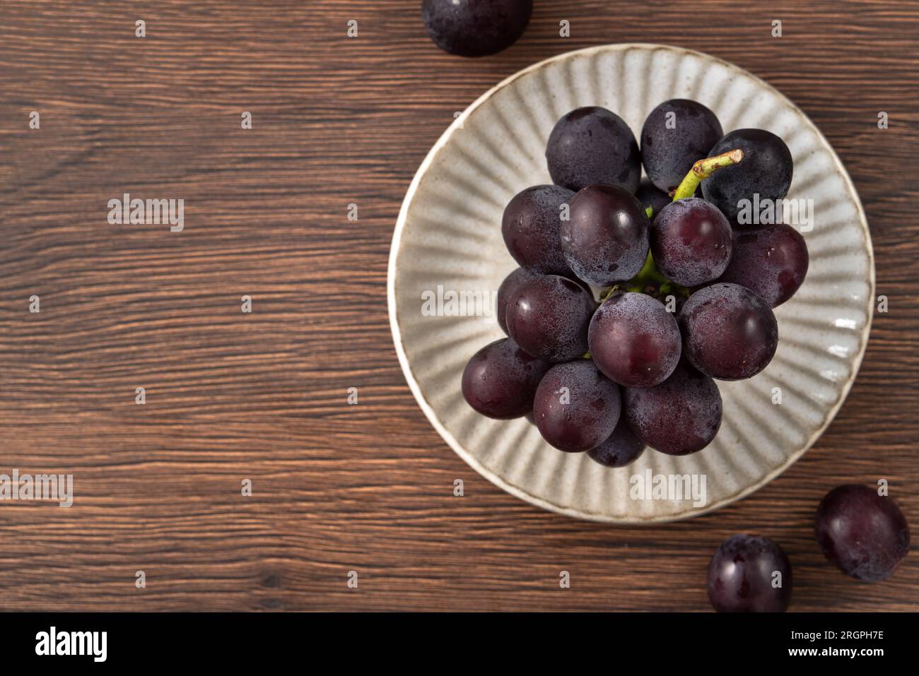 Delicious bunch of purple grapes fruit in a plate on wooden table background. Stock Photo