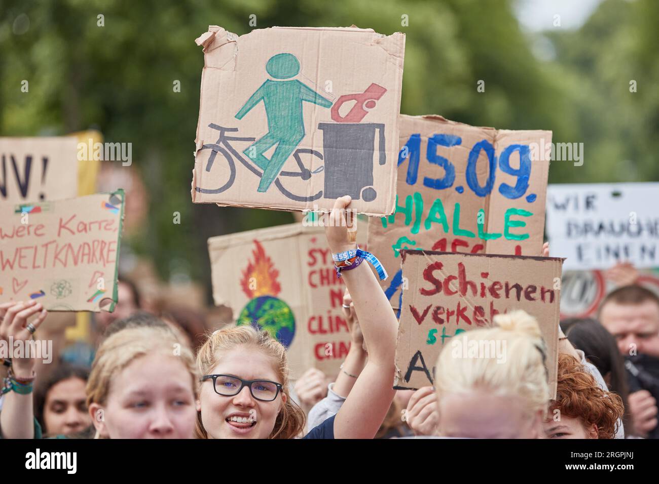 11 August 2023, Lower Saxony, Lüneburg: A participant in a protest march of the climate movement Fridays for Future carries a cardboard sign with a depiction of a cyclist disposing of a car in a trash can. The demonstration through Lüneburg is intended, among other things, to draw attention to the need for the new Hamburg-Hanover rail line. Photo: Georg Wendt/dpa Stock Photo