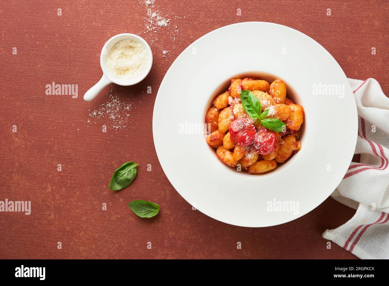Potato gnocchi. Traditional homemade potato gnocchi with tomato sauce, basil and parmesan cheese on kitchen table on red kitchen table background. Tra Stock Photo
