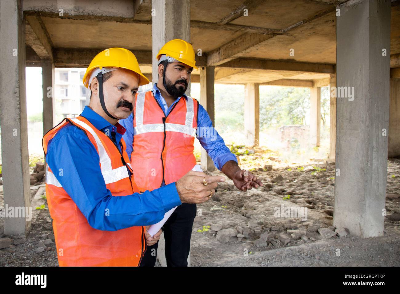 Two Indian female civil engineers or architect wearing helmet and vest working at construction site, Real estate. Stock Photo