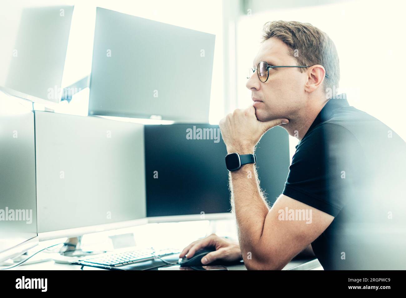 Male stock broker trading online watching charts and data analyses on multiple computer screens. Stock Photo