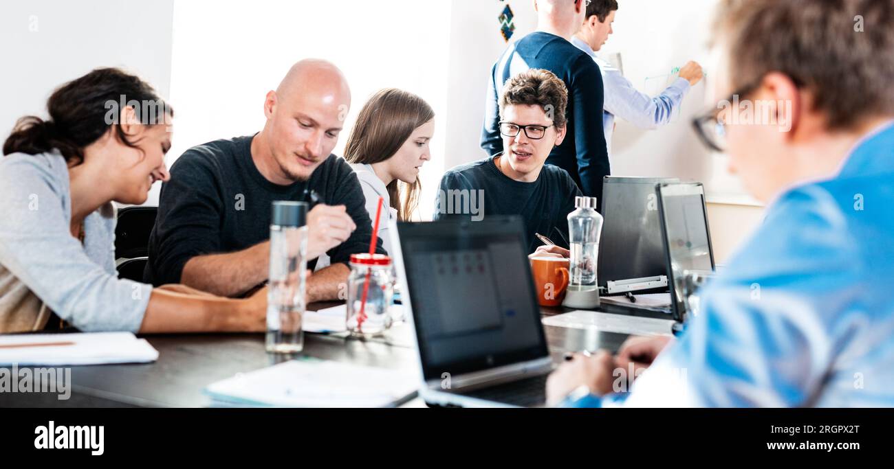 Startup business and entrepreneurship problem solving. Young AI programmers and IT software developers team brainstorming and programming on desktop computer in startup company share office space. Stock Photo