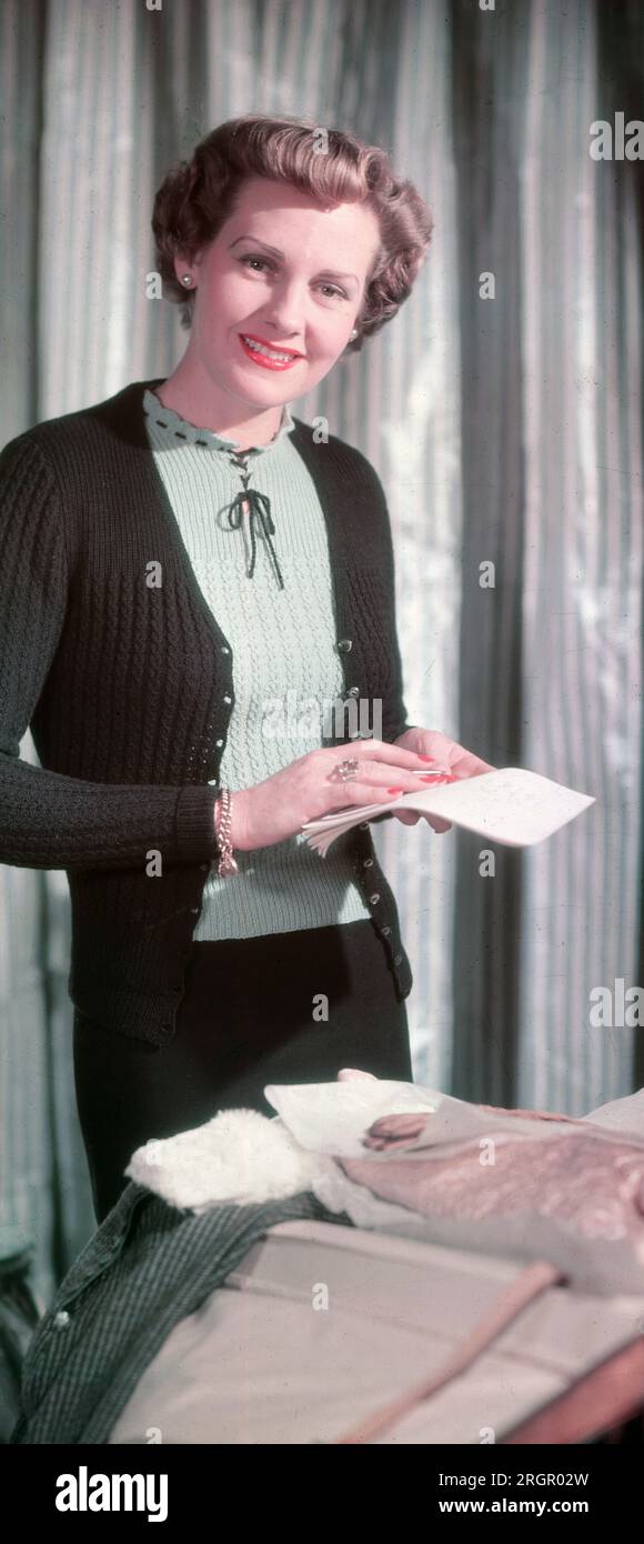 1950s, historical picture showing English fashion in this era....inside a room, an elegant, attractive lady wearing a light woollen cardigan over a delicate blouse, clothes reflecting her feminine, delicate features and refined, sophisticated style, England, UK. The 50s was the decade of the cardigan. Stock Photo