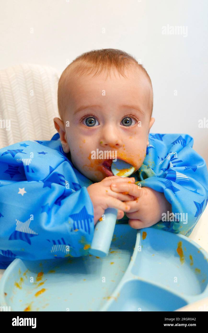 Blue eyed baby eating soup by himself with a silicone spoon Stock Photo