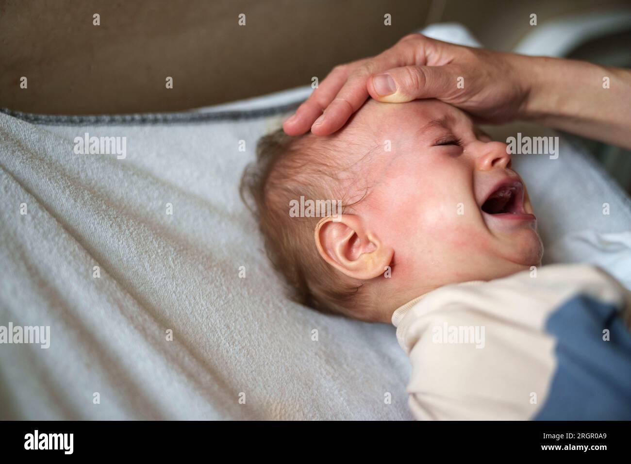 Parent trying to calm an agitated baby crying in pain Stock Photo