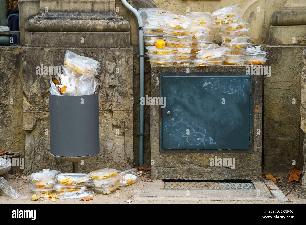 Discarded disposable plastic food containers piled up next to an overflown trash can Stock Photo
